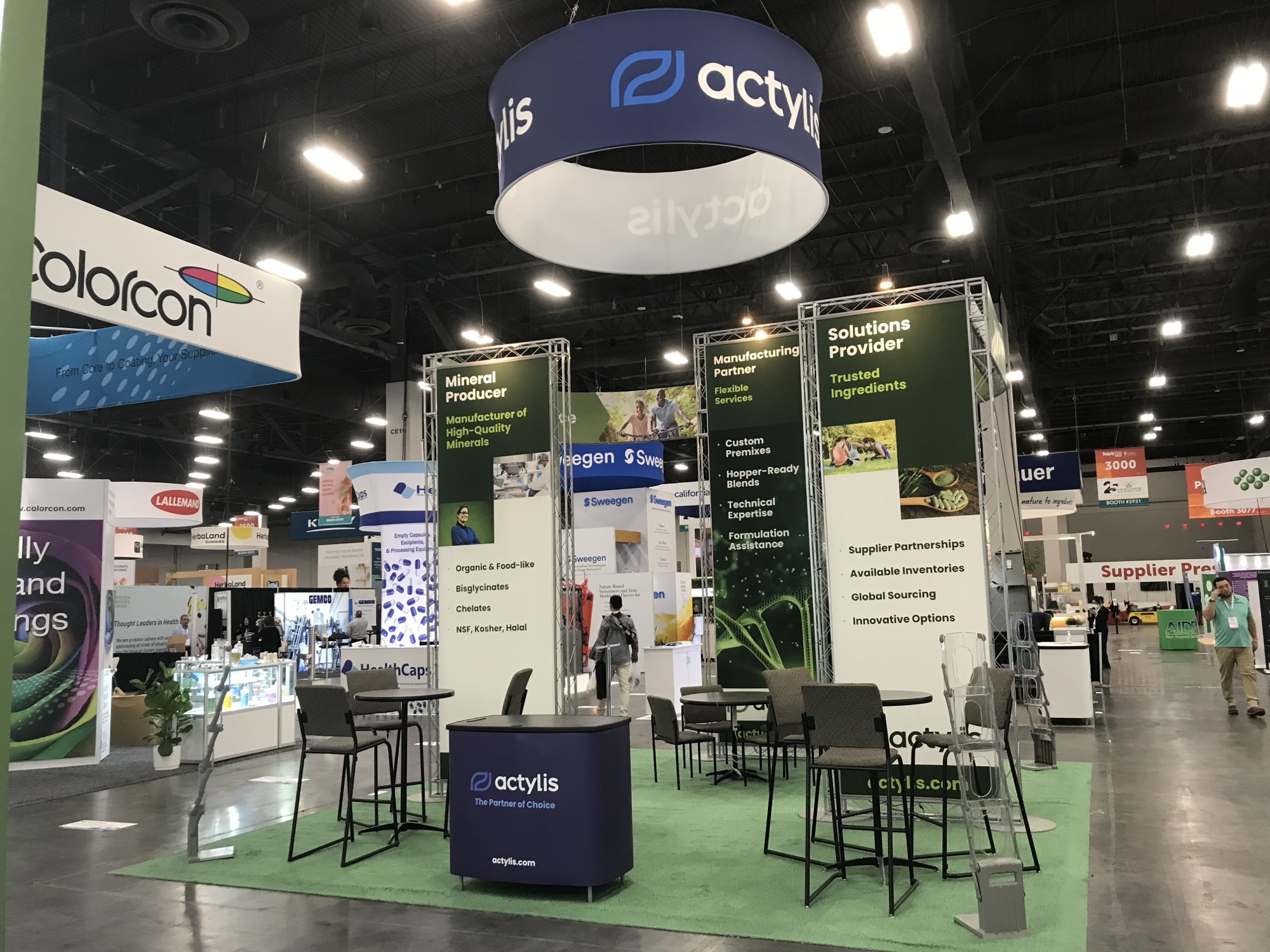 Actylis island booth with circular hanging sign and truss-mounted capability panels at an ingredients trade show
