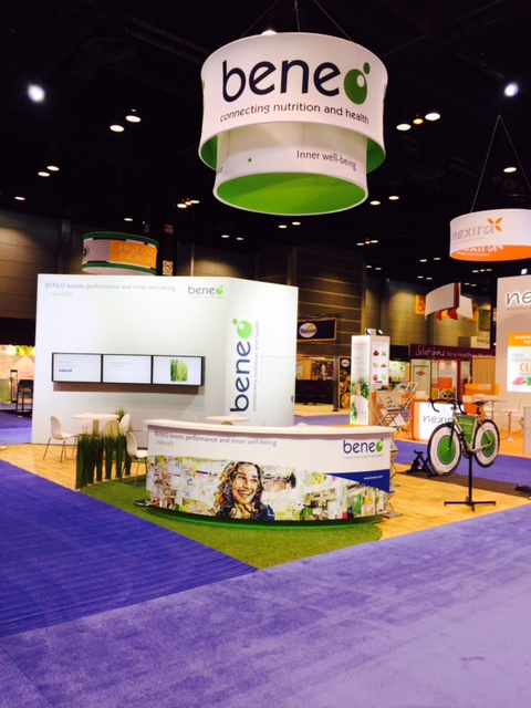 Beneo booth with round hanging sign, turf flooring, and bicycle display at a nutrition trade show