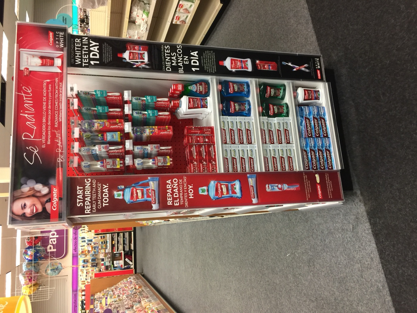 Full-height Colgate Optic White display tower stocked with toothbrushes, toothpaste, and mouthwash in a drugstore aisle