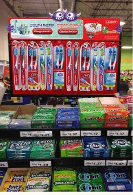 Colgate toothbrush display header installed above the gum shelf at a grocery checkout lane