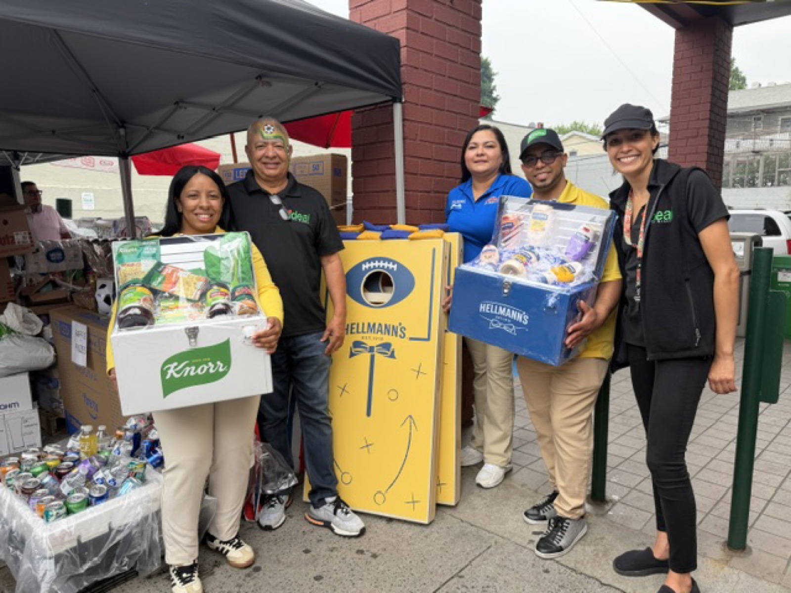 HAP team members and retail partners at a street event holding Knorr and Hellmann's branded prize-pack coolers filled with products, next to a custom Hellmann's cornhole game board