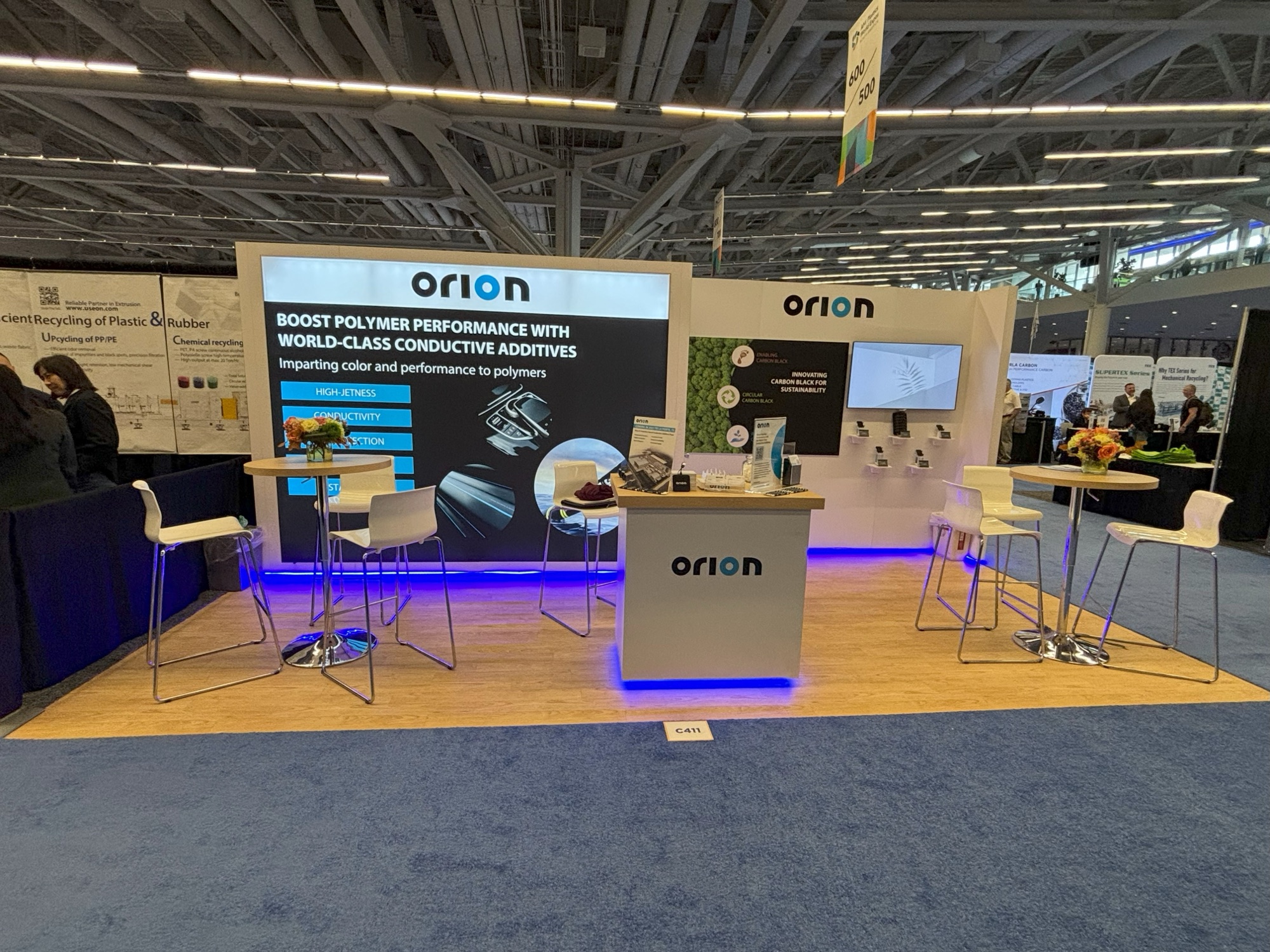 Orion inline booth with white backlit walls, blue accent lighting, and polymer additives graphics