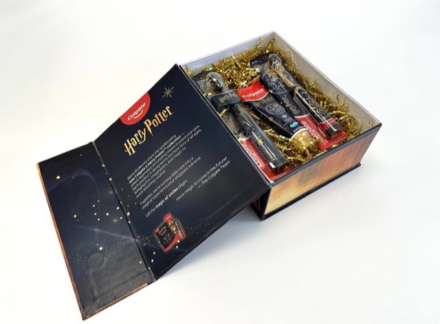 Book-style Colgate Harry Potter gift box opened to show oral care products in gold paper shred