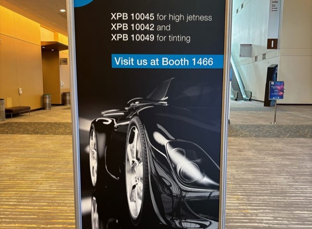Freestanding banner with a black sports car graphic directing convention attendees to a trade show booth