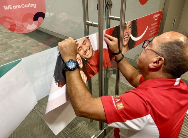 Installer applying Colgate-branded graphics to glass doors at an office entrance