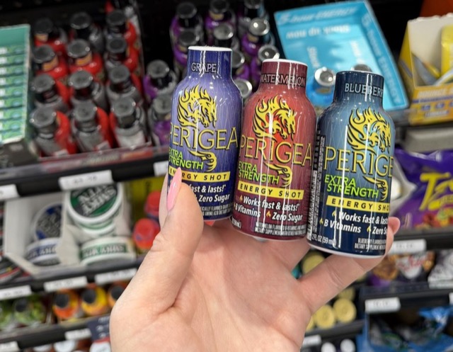 Hand holding three flavors of Perigea Extra Strength energy shots in a store aisle