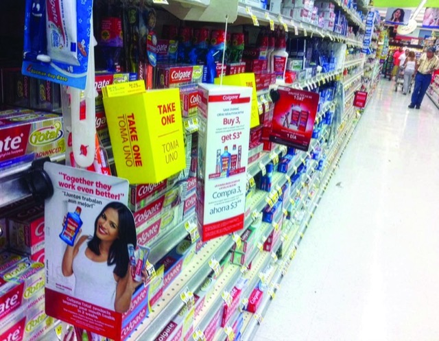 Colgate promotional signs and take-one coupon boxes displayed along a grocery toothpaste aisle