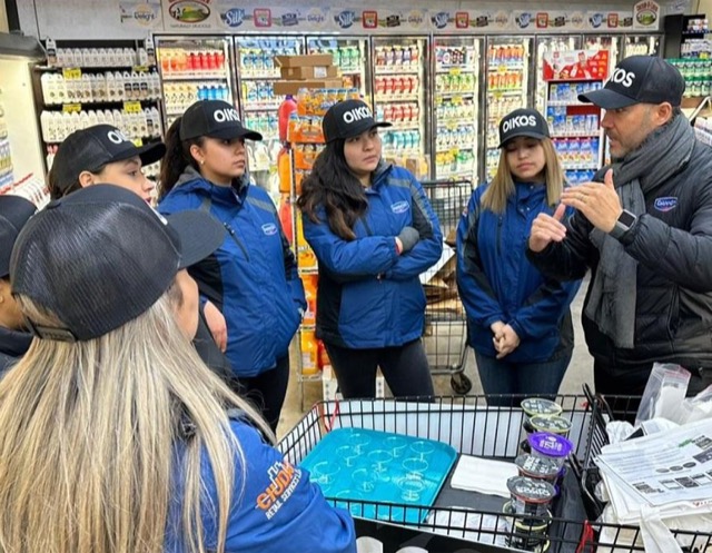 Field marketing team in Oikos caps gathered around a sampling cart inside a grocery store