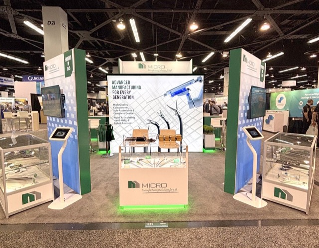 MICRO exhibit booth with backlit graphic wall, product display tables, and video monitors